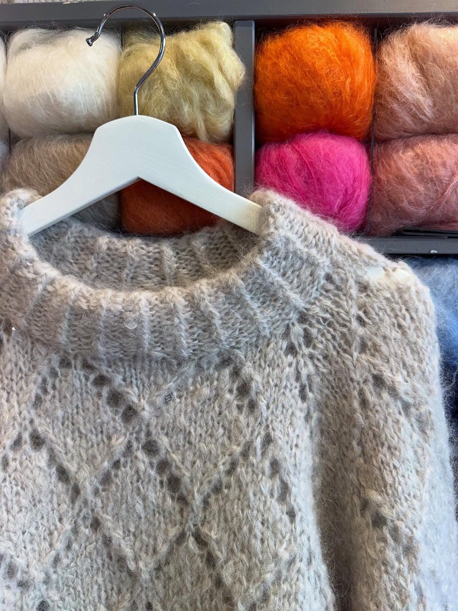 Lys hullmønstret genser i tykk mohair på kleshenger foran nøster i oransje og rosa