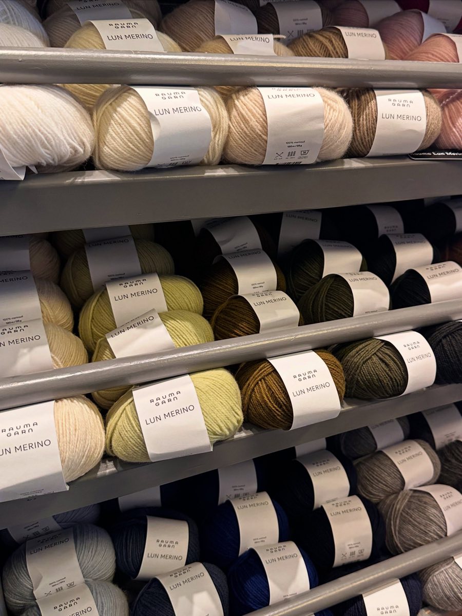 Hyller fulle av garnnøster i hvitt, gult, grått og blått inne i butikken