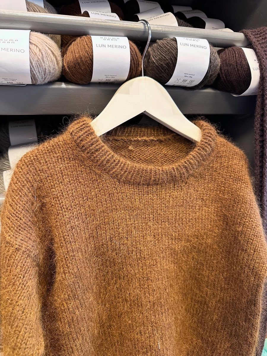 Brun Holger Sweater i mohair henger på en kleshenger foran garnhyllene
